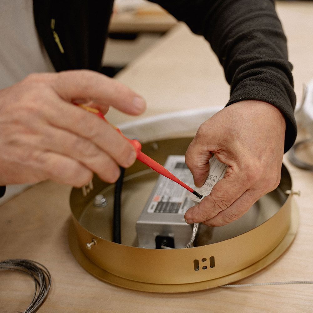 Techniker überprüft die elektrische Verkabelung der s.luce Ring Hängeleuchte auf einem Tisch.