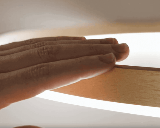 Hand berührt den Holztischrand einer modernen Lampe mit sanfter Beleuchtung.