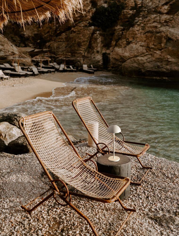 Zwei Liegestühle am Strand mit einer eleganten Rose LED Außentischleuchte 3000K IP54 auf einem Tisch.