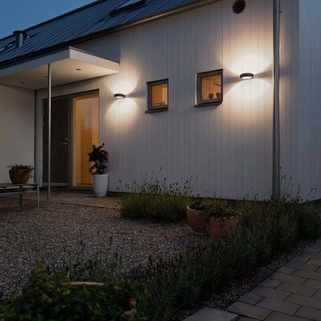 Rovigo LED utendørs vegglampe antrasitt, opalt akrylglass installert på et moderne hus om natten.
