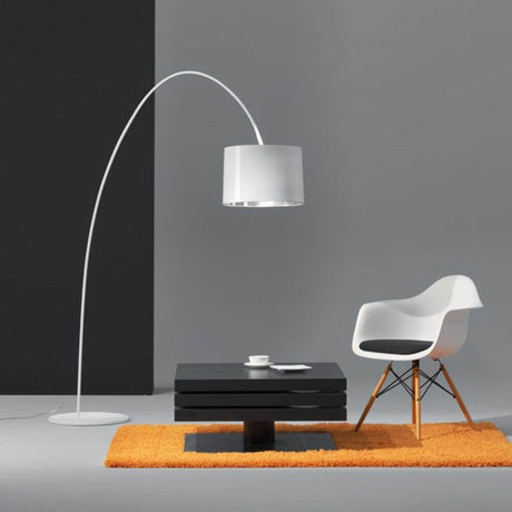 Roxx Bogenleuchte 188cm mit Schirm Weiß über einem schwarzen Tisch und einem weißen Stuhl auf einem orangefarbenen Teppich.