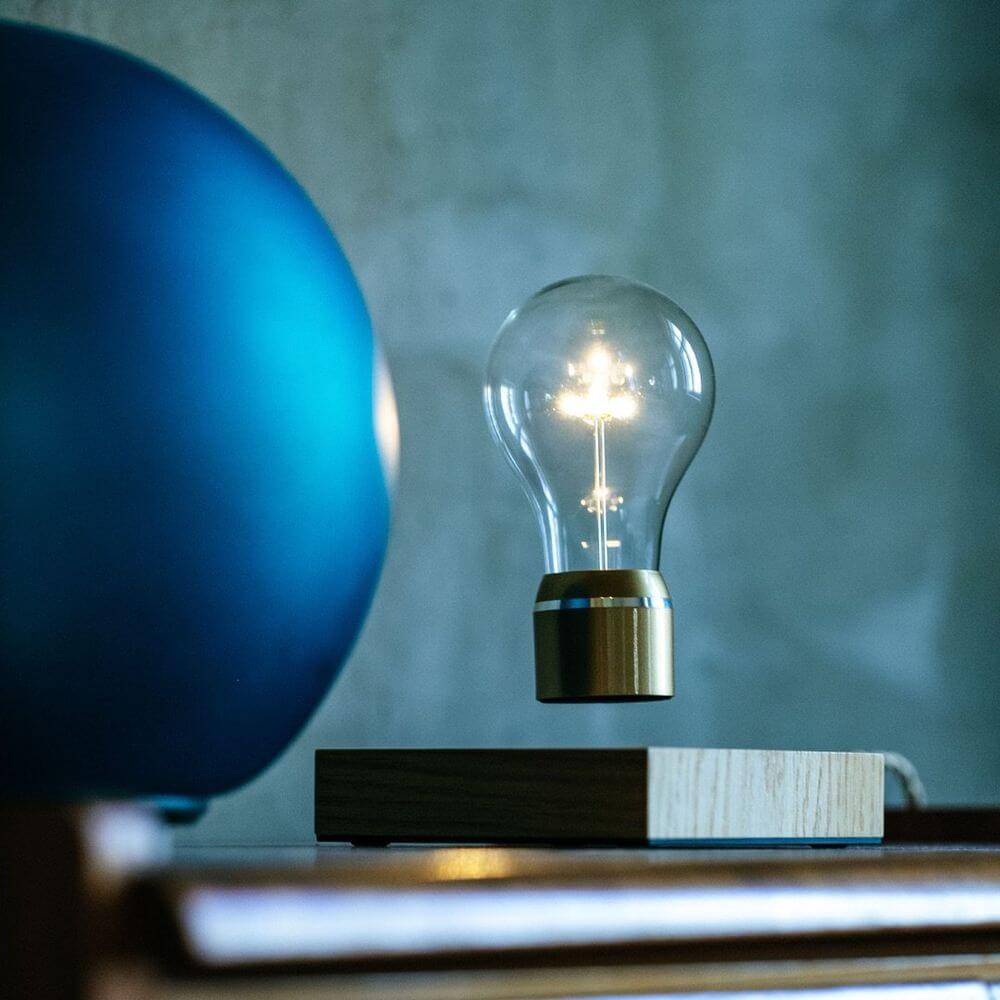 LED-Dekotischleuchte schwebende Glühbirne auf einem Holztisch, umgeben von modernen Dekorationsgegenständen.