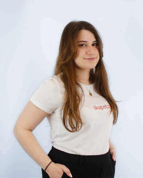 Junge Frau in T-Shirt mit "skapezt" Aufdruck, steht lächelnd vor weißem Hintergrund.