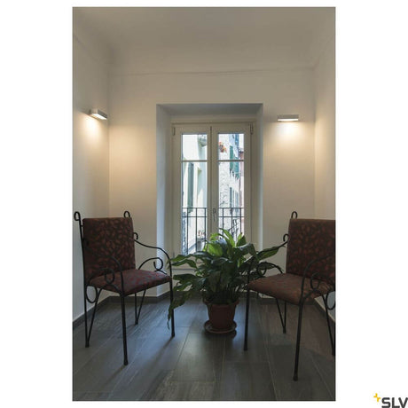 Andreas Qt-De12 Wall Light Grey installed in a modern room with plants and chairs.