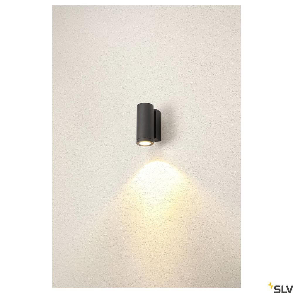 Enola LED Wandaufbauleuchte Round S Single Outdoor Anthrazit an einer Wand montiert, beleuchtet mit warmem Licht.