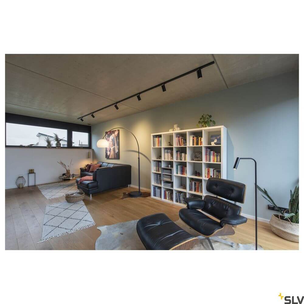 Fenda Bow Basis E27 Bogenleuchte Schwarz (ohne Schirm) in modernem Wohnzimmer neben Regal und Lounge-Sessel, stabiles Bodenmodell mit chromfarbenem Bogenarm