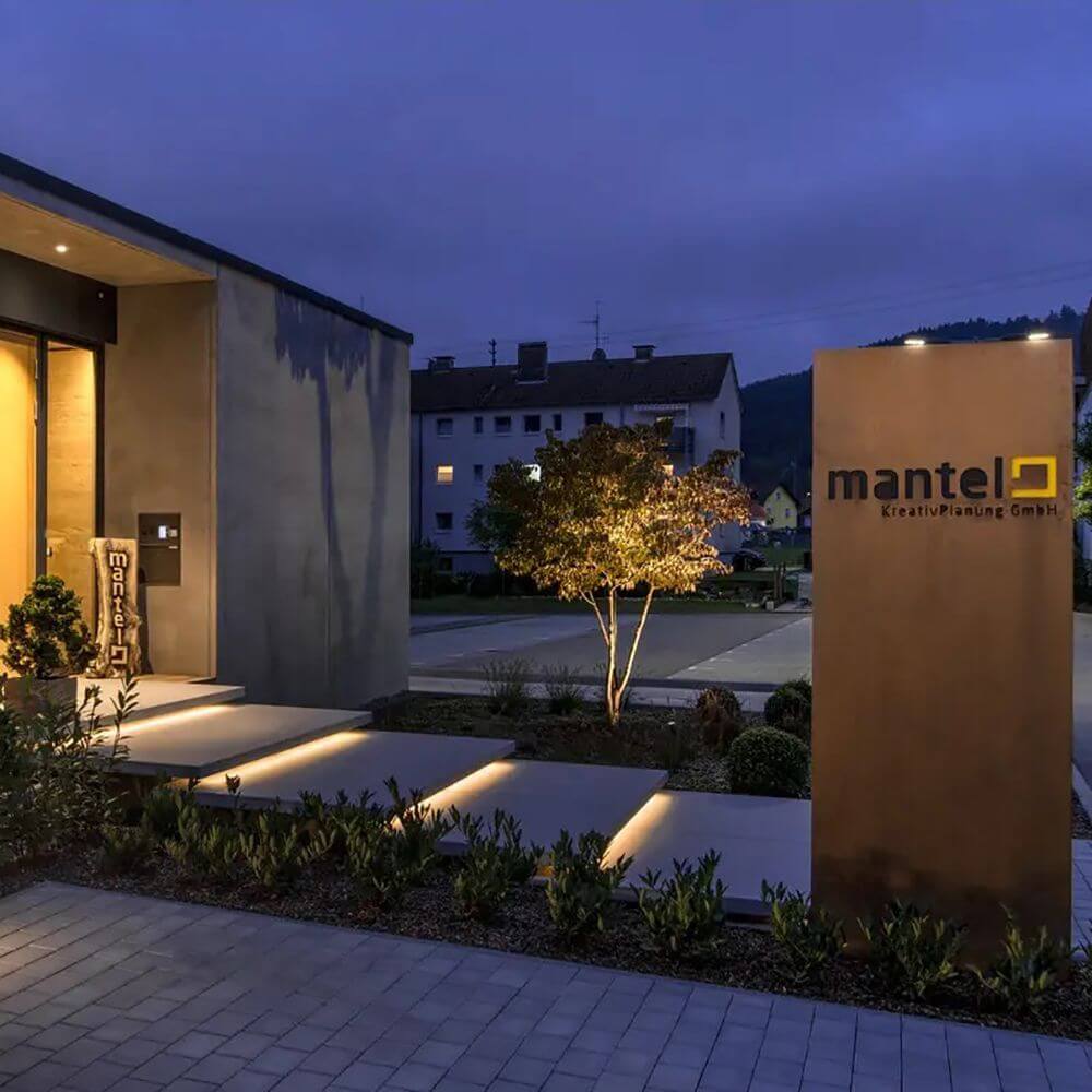 Eingangsbereich der Mantel KreativPlanung GmbH bei Nacht, mit beleuchtetem Weg und modernem Design.