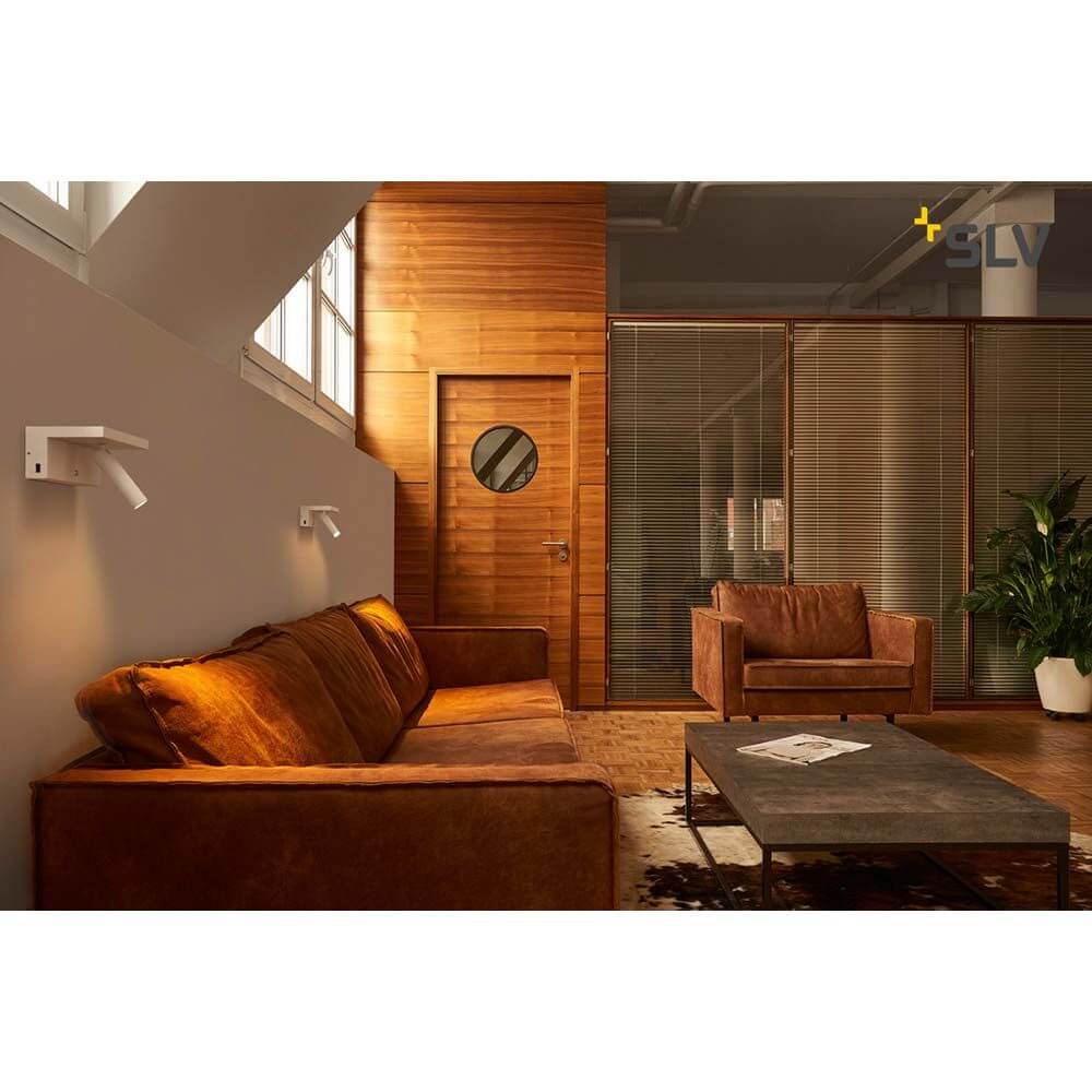 Karpo Bedside LED Wandaufbauleuchte Weiß in modernem Wohnraum mit Sofa und Holzdetails.
