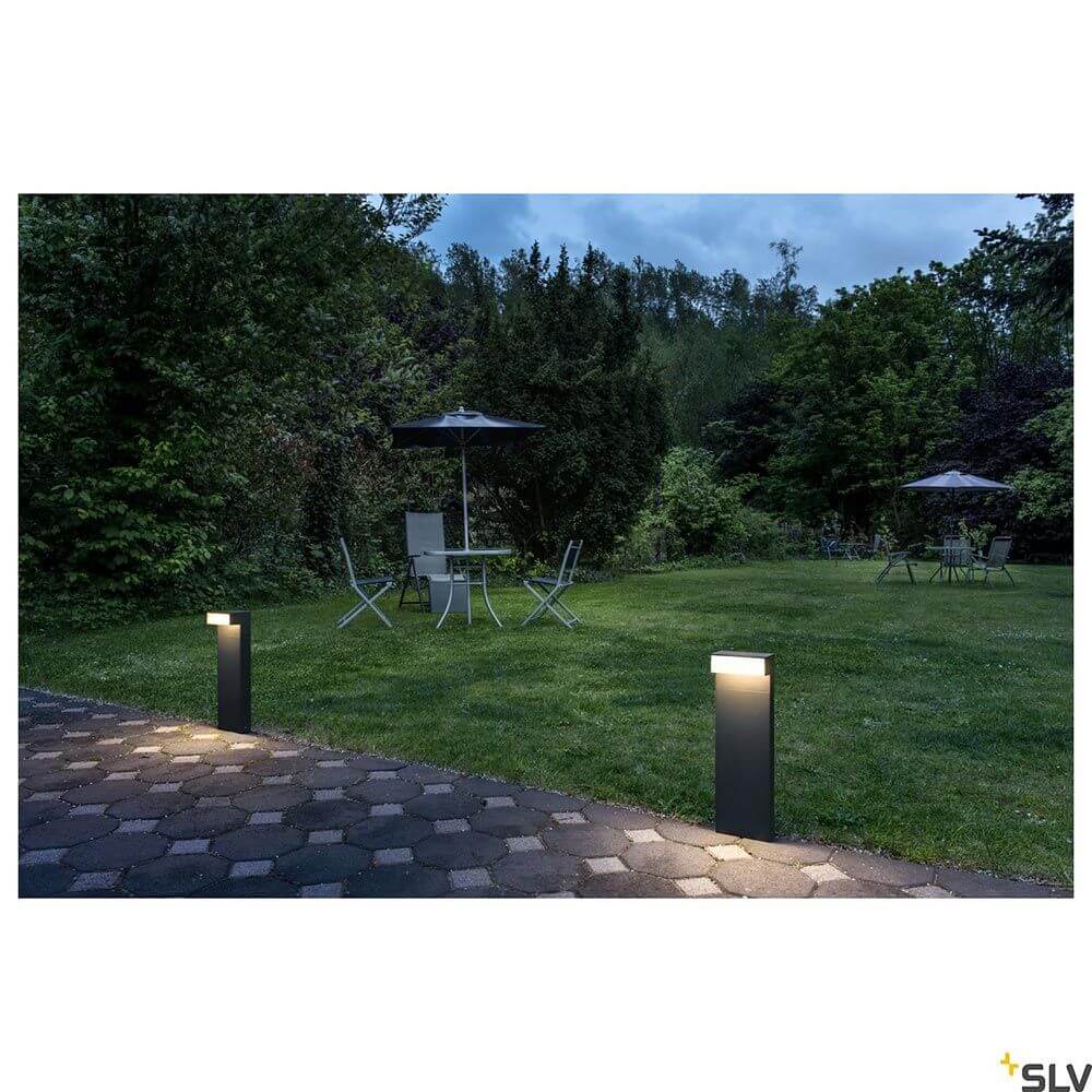 L-Line LED Pollerleuchte Pole Anthrazit CCT IP65 leuchtet Gartenweg bei Nacht, umgeben von Stühlen und Sonnenschirm.