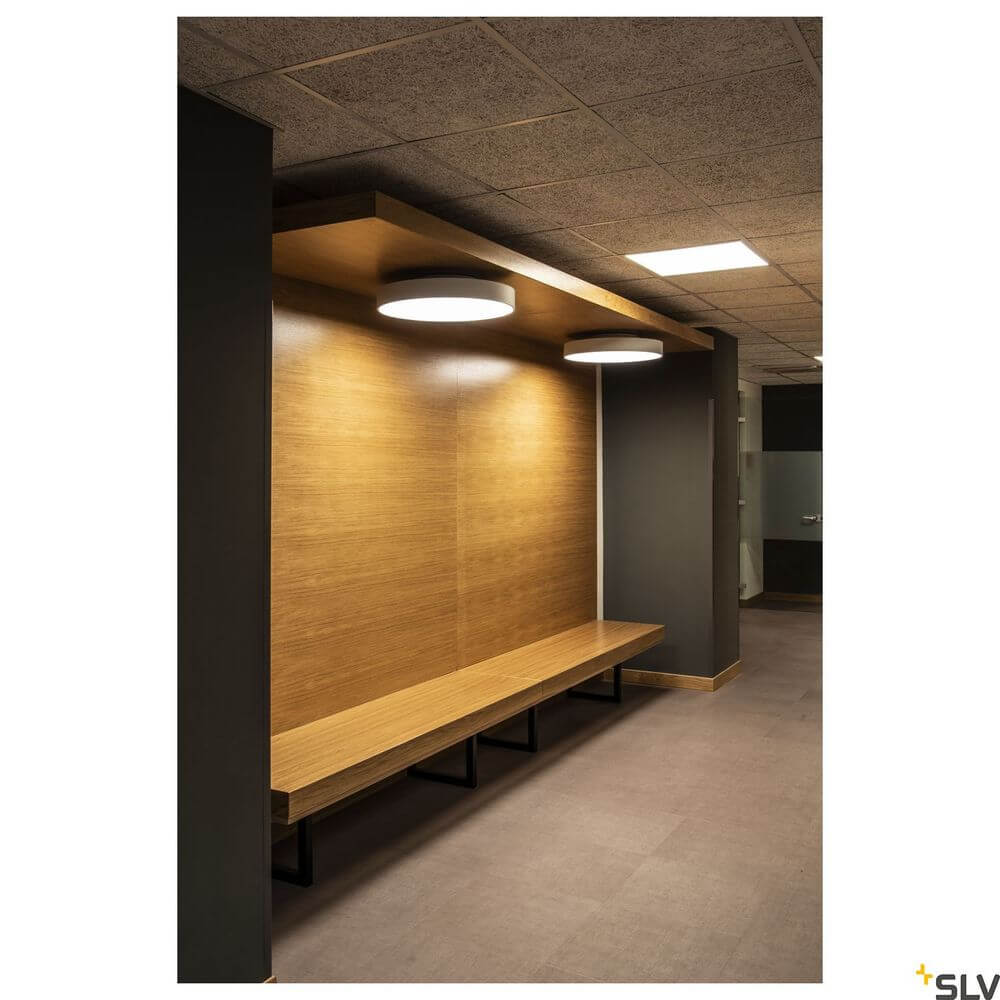 LED Panel 620 Deckenleuchte Weiß 3000K an moderner Wand mit Holzregal im Innenraum.