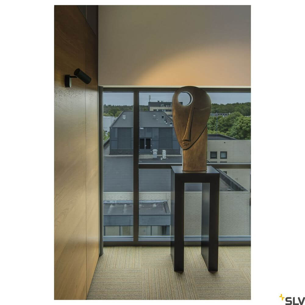 Noblo I Strahler 2700K Schwarz beleuchtet eine moderne Kunstskulptur in einem eleganten Raum.