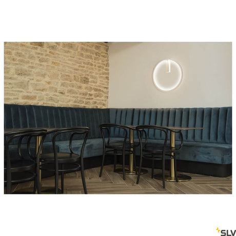 One 60 vegglampe Dali 3000-4000K hvit på en vegg i en stilfull kafé med blå benkpolstring.