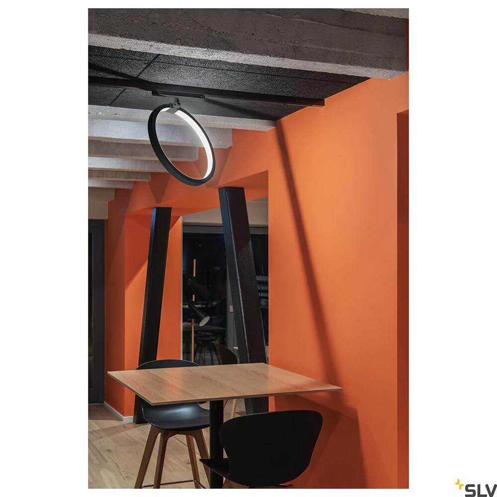 One LED Systemleuchte 3-Phasen Dali Ø 40cm in modernem Design über einem Tisch an einer orangefarbenen Wand.