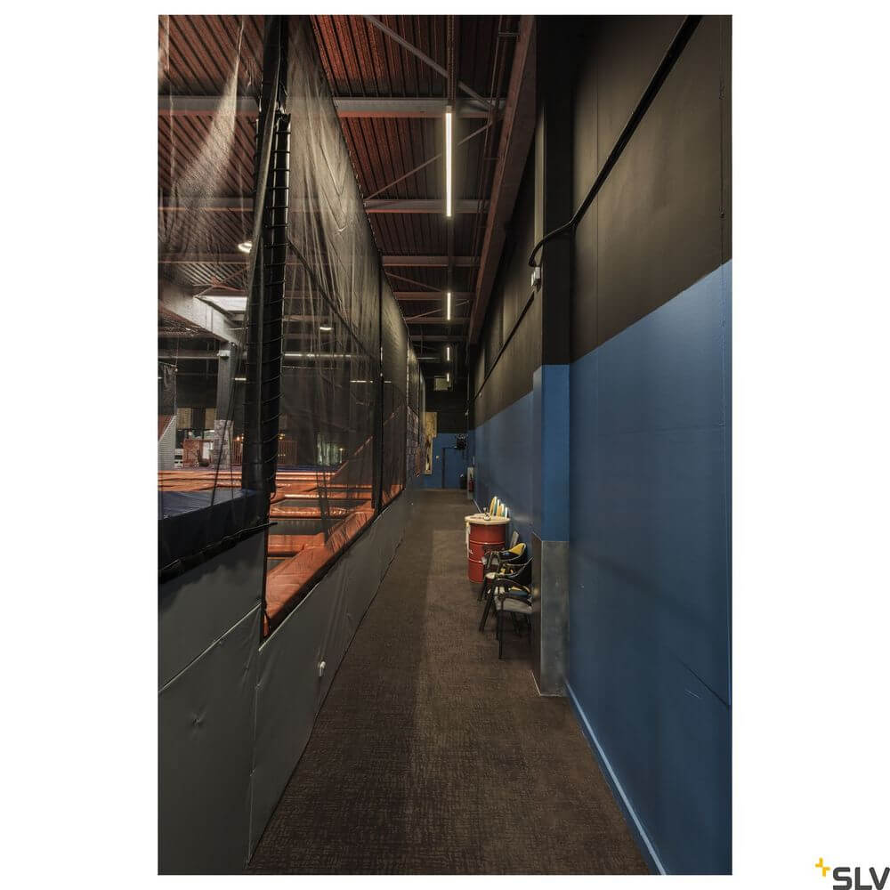 Lange Halle mit blauen und schwarzen Wänden, Netztrennwänden und Tischtennisplatten in einem Sportzentrum.