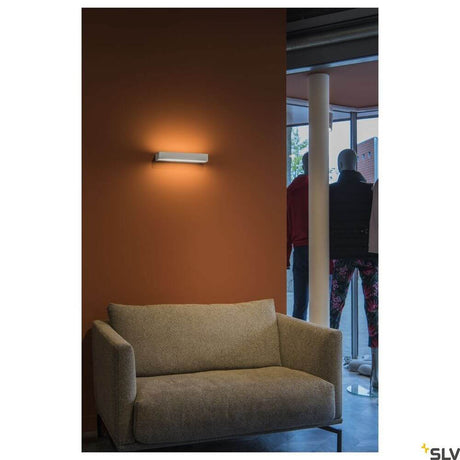 Sedo 7 wall light 3000K white on a wall above a beige sofa, modern interior lighting.