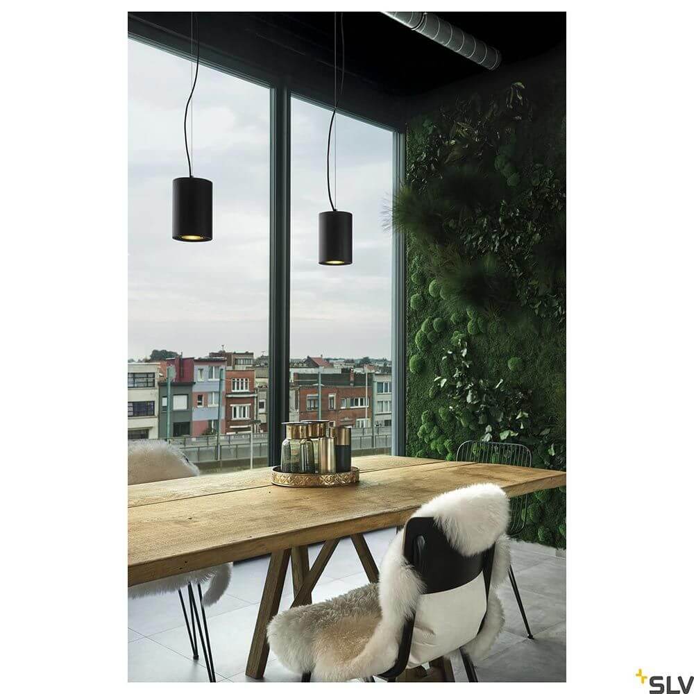 Moderne Einrichtung mit Supros LED Pendellampe über einem Holzstammtisch in einem lichtdurchfluteten Raum.