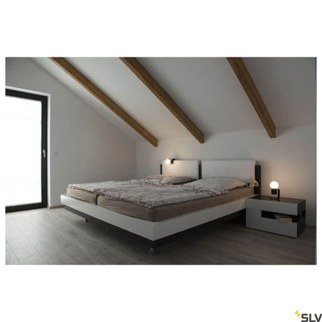 Tonila Mobile Akku-Tischleuchte Schwarz neben einem modernen Bett in einem stilvollen Schlafzimmer.
