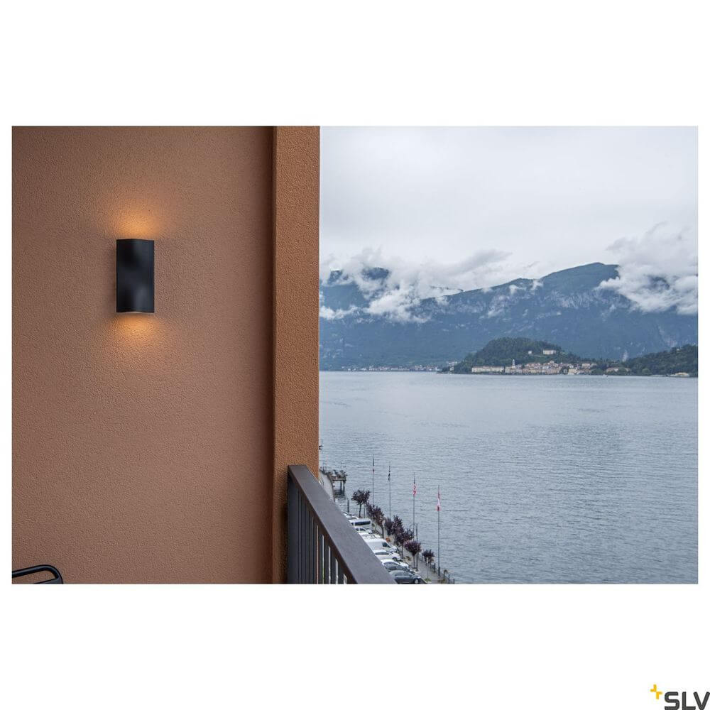 Vilua Up & Down Außen-Wandlampe LED Anthrazit IP54, montiert an einer Wand mit Blick auf den See.