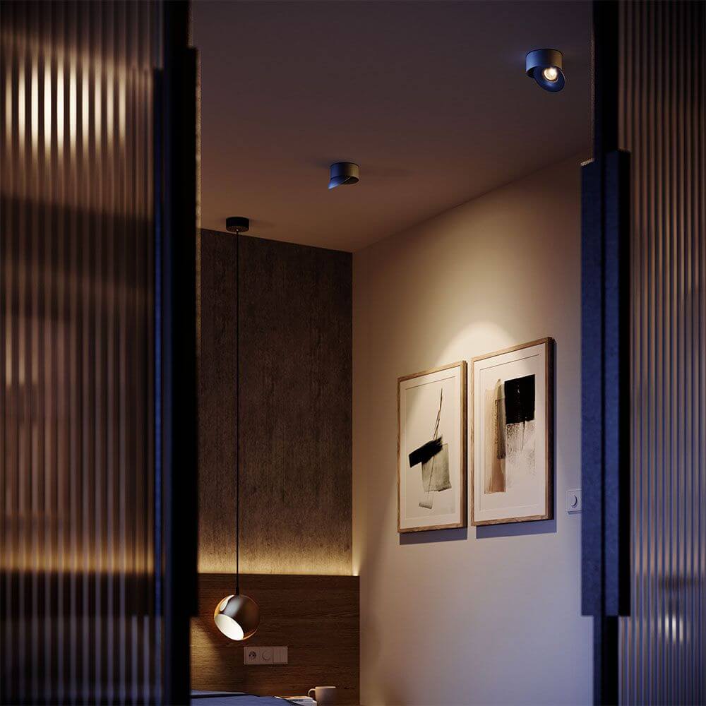 Modernes Schlafzimmer mit drehbarem LED-Deckenstrahler, Kunstwerken und gemütlicher Beleuchtung.