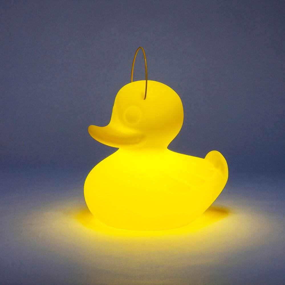 Schwimmfähige Akku-LED-Leuchte Duck-Duck S Gelb in Form einer leuchtenden gelben Ente auf einem blauen Hintergrund.
