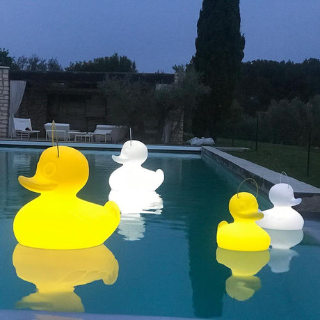 Lámpara de batería flotante LED Duck-Duck S Amarilla en la piscina por la noche con otras lámparas de pato de plástico.