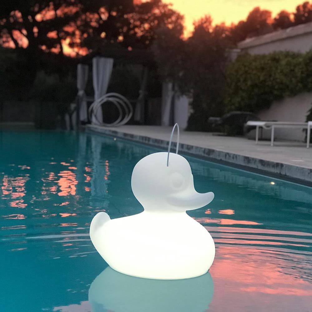 Schwimmfähige Akku-LED-Leuchte Duck-Duck S Weiß, Designleuchte in Form einer Ente schwimmt im Pool bei Sonnenuntergang.