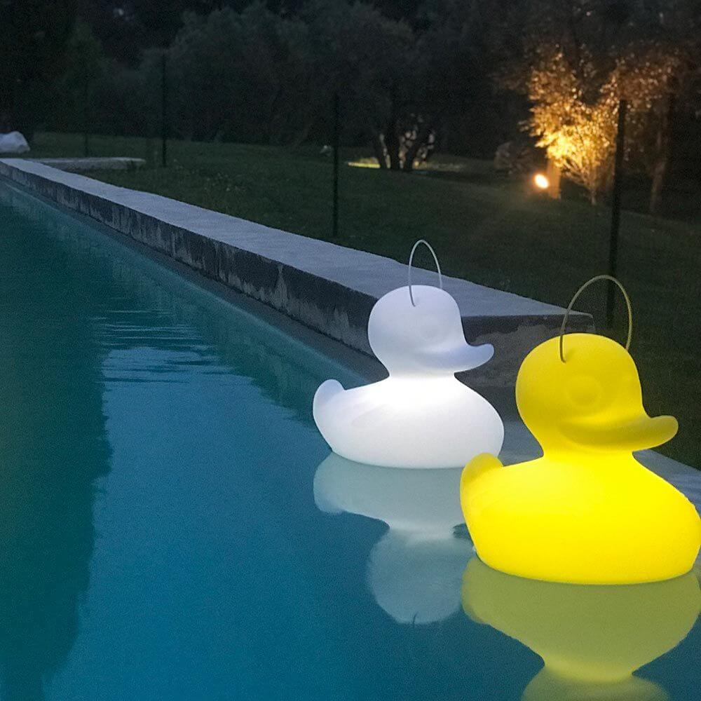 Schwimmfähige Akku-LED-Leuchten in Entenform, eine weiße und eine gelbe, am Rand eines Pools bei Nacht.