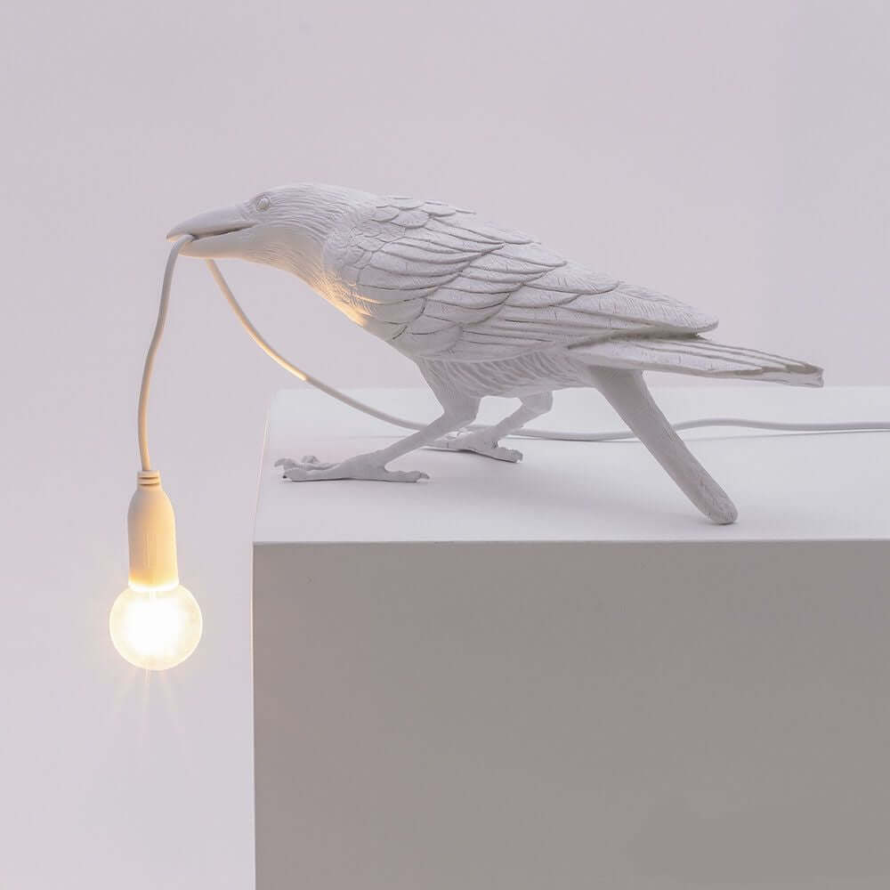 Seletti Bird Außen-Tischleuchte gebeugt mit Rabe und glühbirne auf einem Tisch.