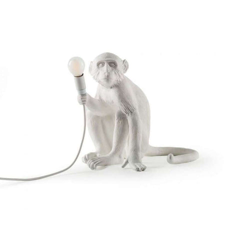 Seletti Monkey bordlampe sittende hvit som et оригинalt design med dyremotiv og lampe i hånden.