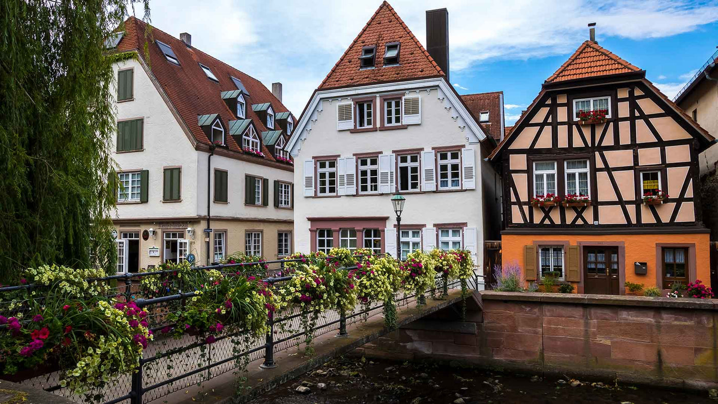 Schöne Fachwerkhäuser und bunte Blumen auf einer Brücke in einer malerischen Stadt.