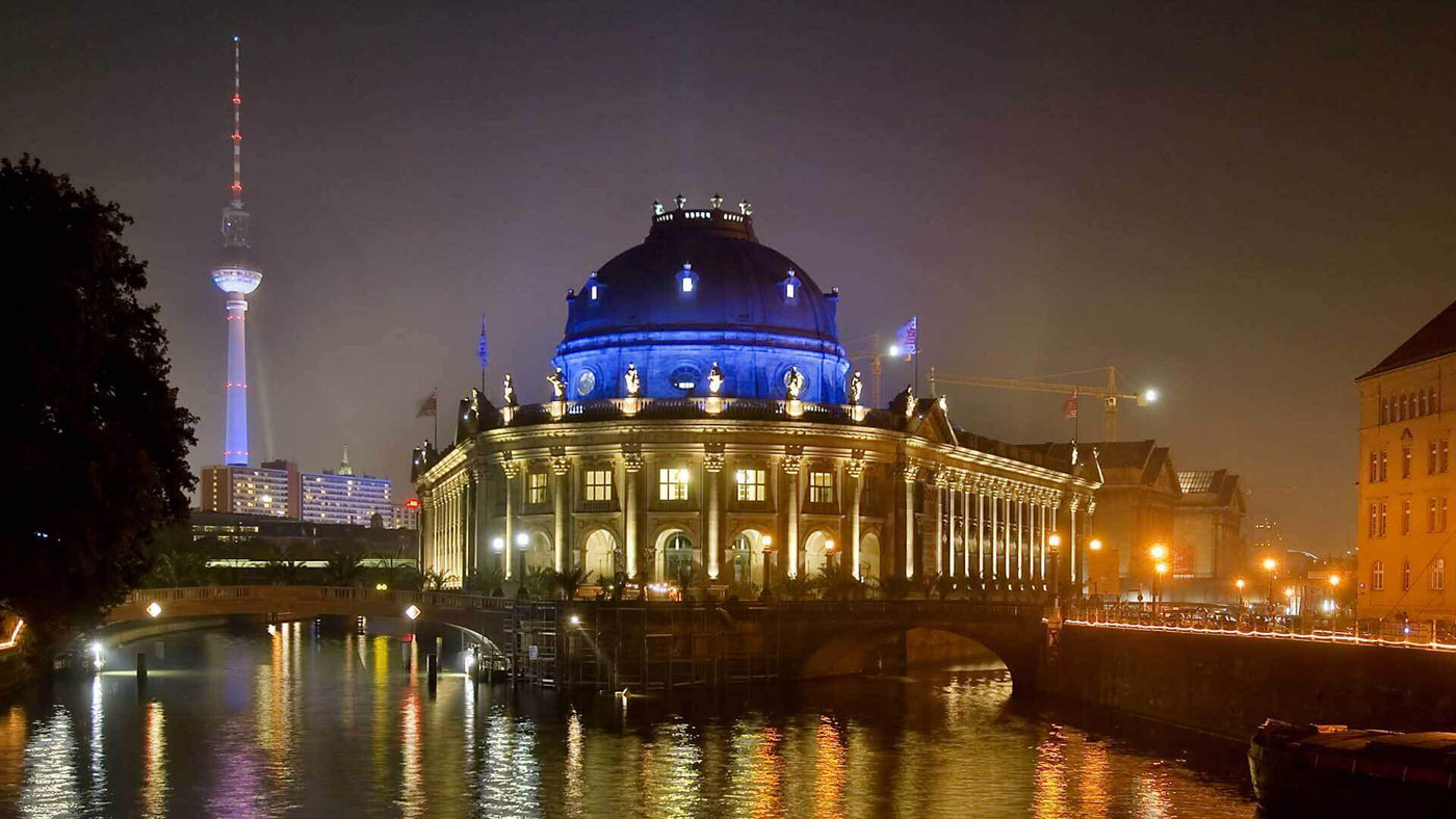 Berliner Dom bei Nacht mit blauem Licht, Fernsehturm im Hintergrund, reflektiert im Wasser.
