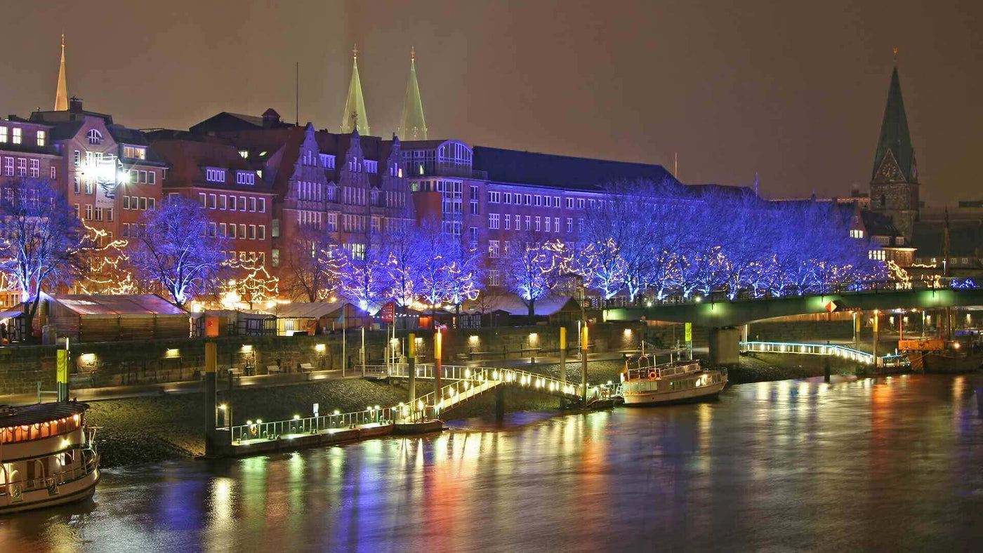 Nachtansicht der Bremer Altstadt mit beleuchteten Bäumen und Booten am Wasser, magische Stimmung.
