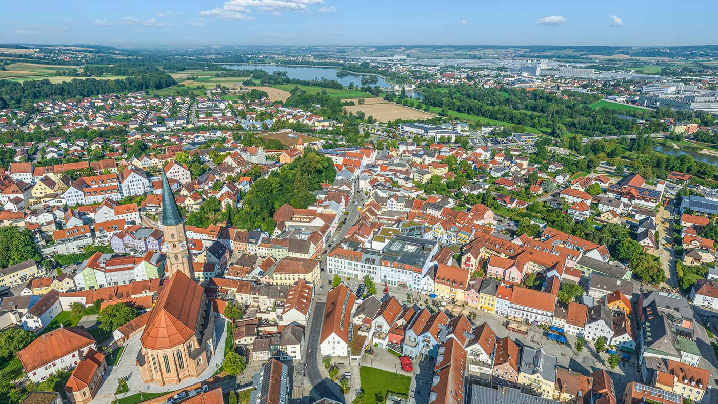 Luftaufnahme einer Stadt mit bunten Häusern und Kirchen im Vordergrund, umgeben von Natur.