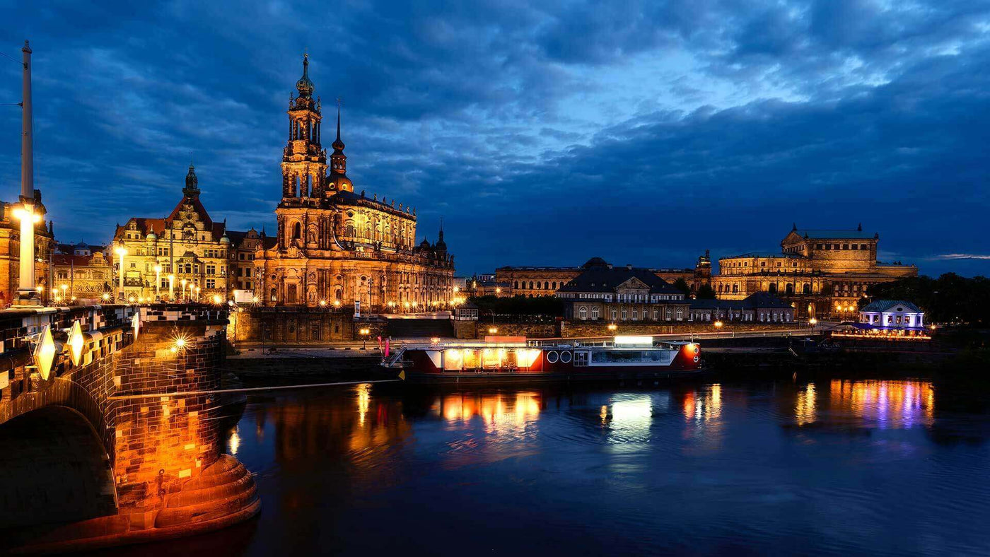 Dresden bei Nacht: Beleuchtete Gebäude am Elbufer unter dramatischem Himmel.