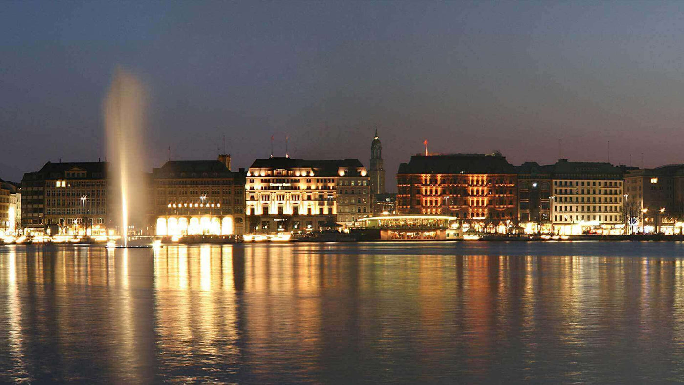 Abendansicht des Genfer Sees mit beleuchteten Gebäuden und dem berüchtigten Wasserspeier.