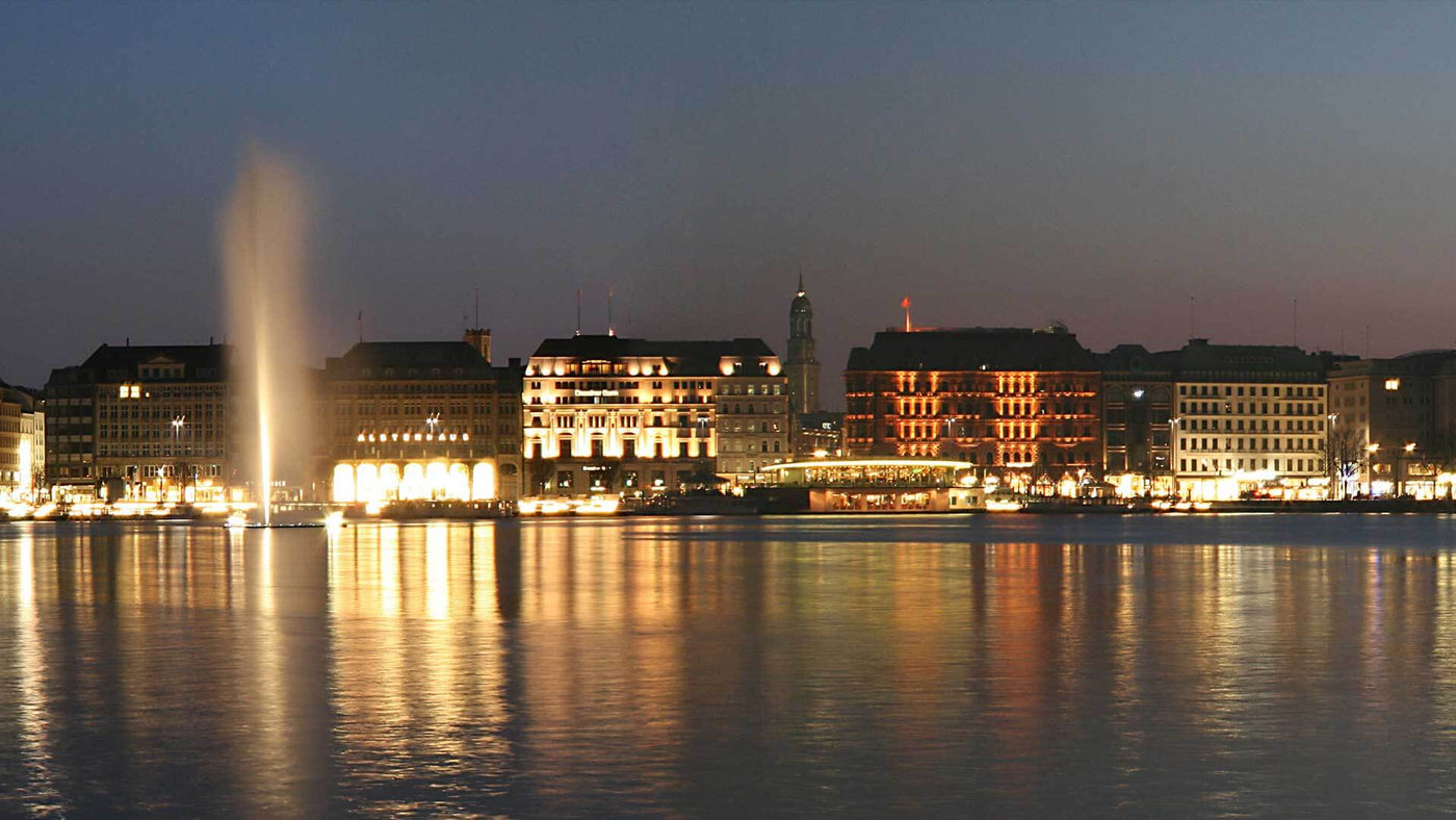 Abendansicht des Genfer Sees mit beleuchteten Gebäuden und dem berüchtigten Wasserspeier.