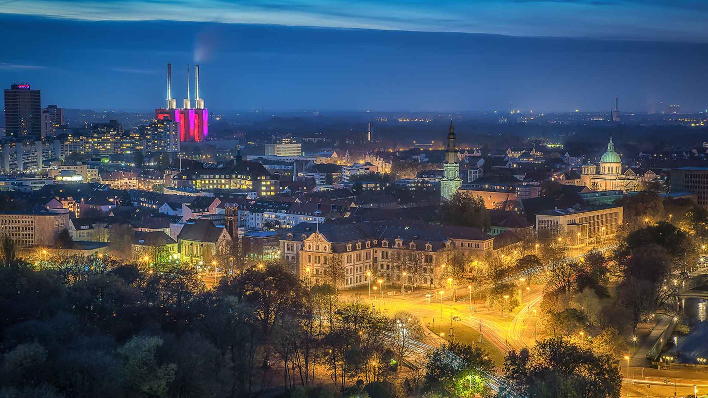 Panorama der Stadt bei Nacht mit beleuchteten Gebäuden und Industrieanlagen, inklusive den lila Türmen.