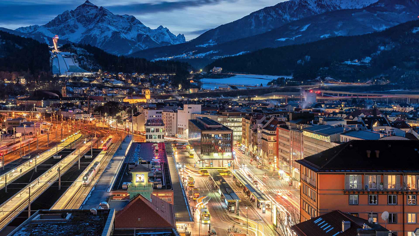 Abendpanorama von Innsbruck mit schneebedeckten Bergen und beleuchteten Straßen.