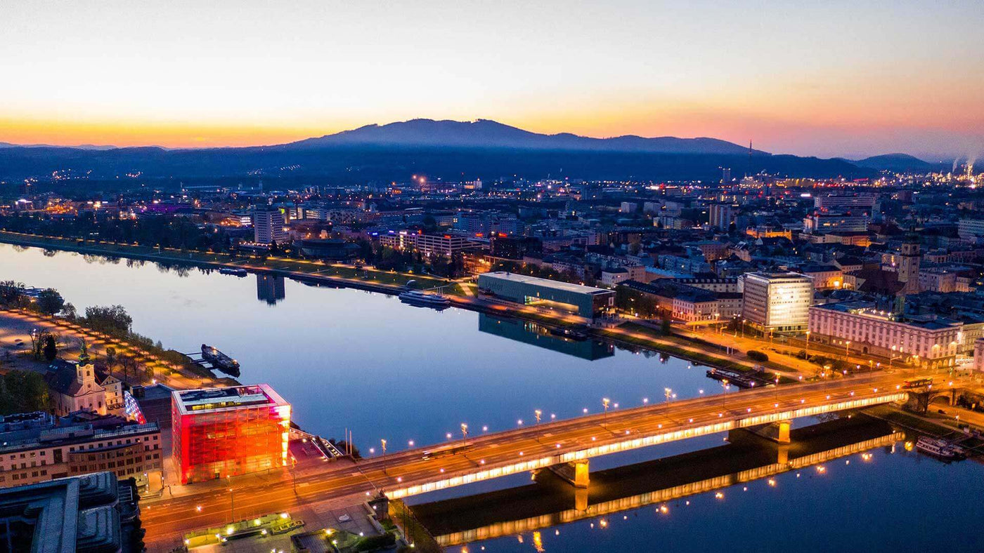 Luftaufnahme einer Stadt bei Sonnenuntergang, die Brücke und der Fluss sind gut sichtbar.