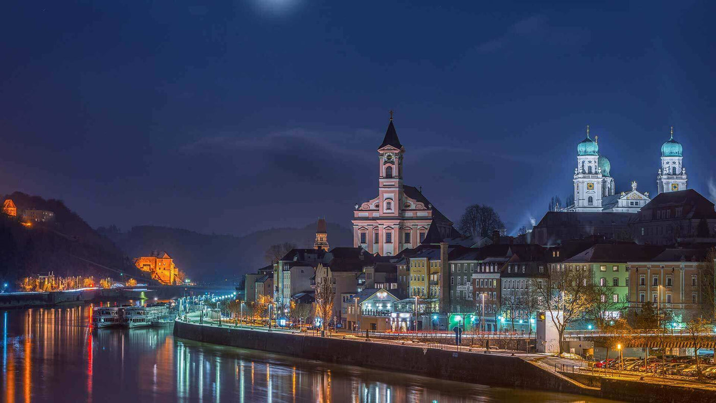 Nachtansicht von Stadt am Fluss, beleuchtet von Mondlicht und Stadtlichtern, historische Gebäude und Kirche.
