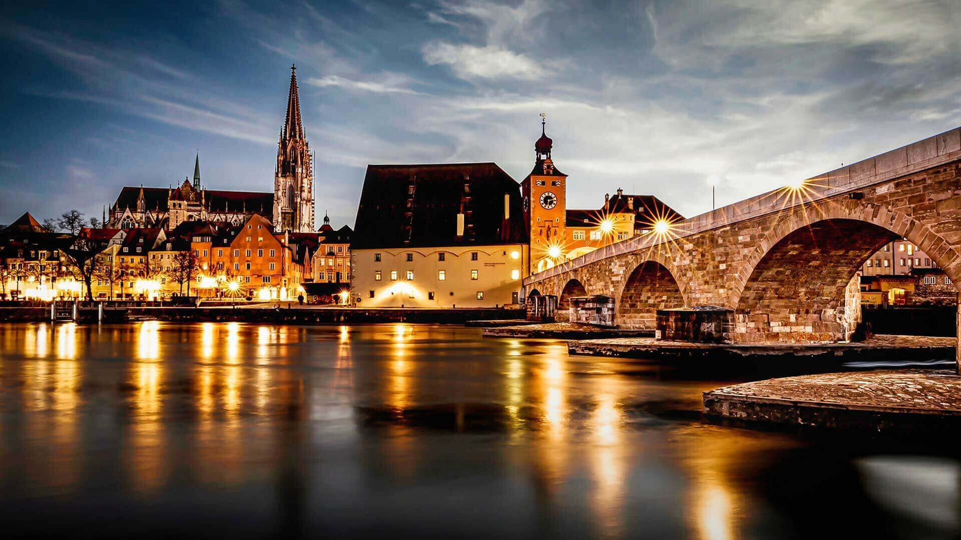 Abendansicht der Stadt Regensburg mit der Steinernen Brücke und historischen Gebäuden am Wasser.