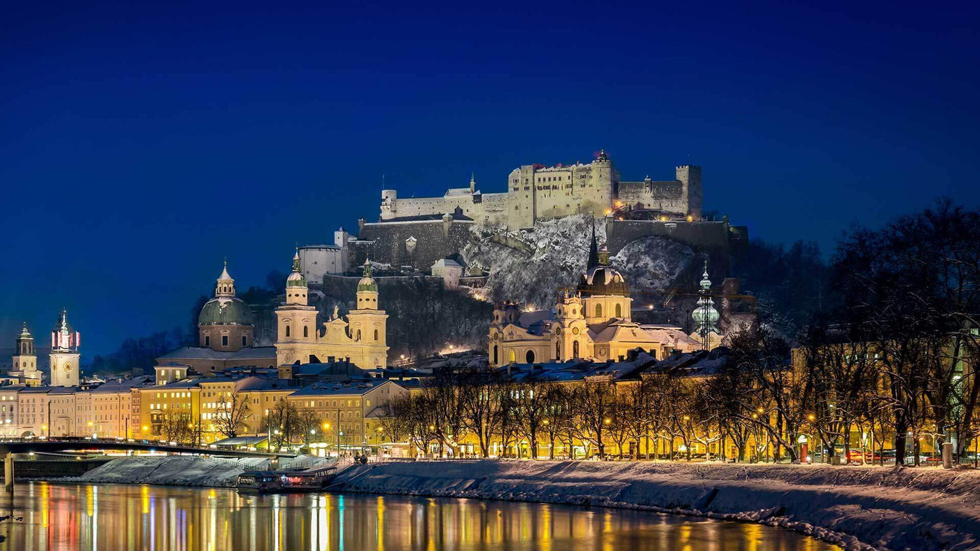 Blick auf die Festung Hohensalzburg und die Salzach bei Nacht, beleuchtet und winterlich.