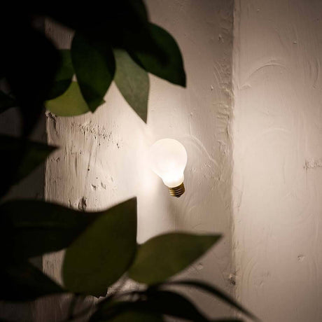 Slamp Einbau-Wandlampe Glühbirne Idea Applique Weiß an einer Wand mit Pflanzen im Vordergrund.