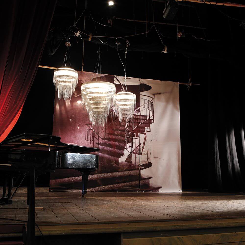 Slamp Hängelampe Ceremony Large Rauchfarben über einem Klavier auf einer Bühnenkulisse.