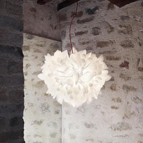 Slamp Pendelleuchte Veli Foliage Weiß in skulpturalem Design, aufgehängt in einem Raum mit Steinwand.