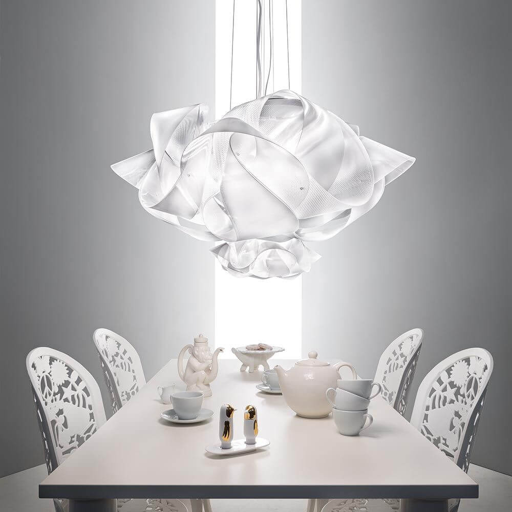 Slamp Hängeleuchte Fabula Large Prisma Transparent über einem eleganten Esstisch mit weißen Stühlen und Geschirr.