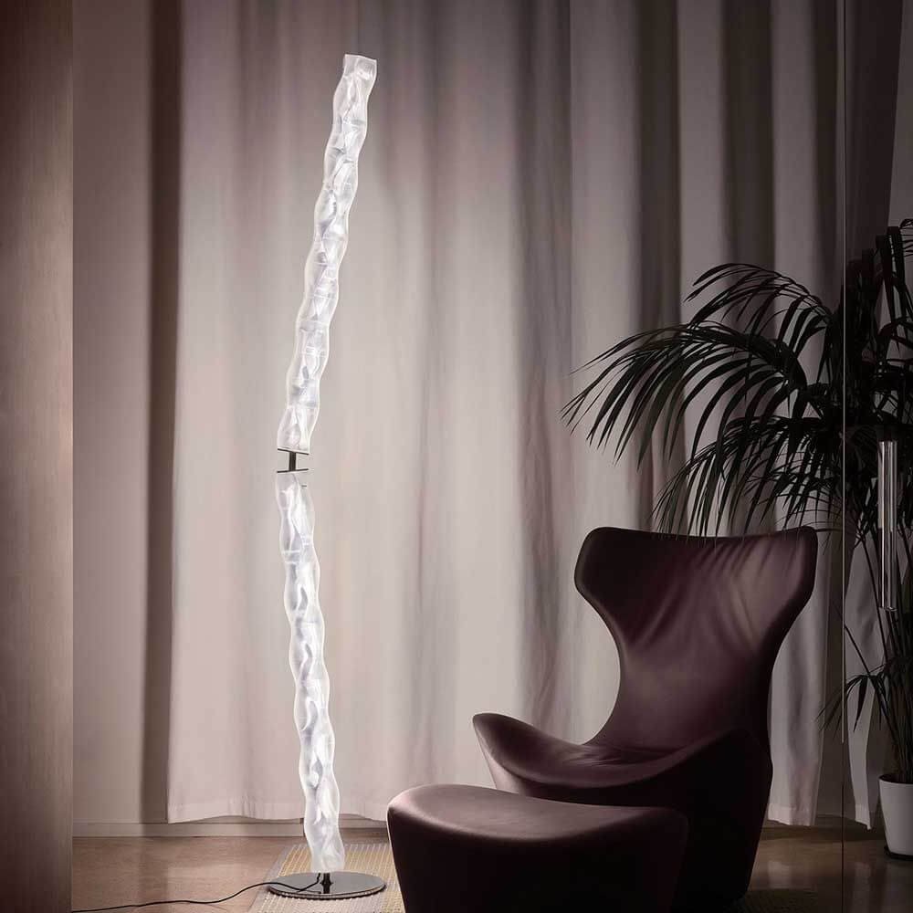 Slamp Hugo Stehleuchte 207cm aus Lentiflex-Kunststoff neben einem modernen Sessel in einem gemütlichen Raum.