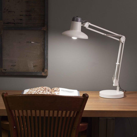 Snap Office Schreibtischlampe auf einem Schreibtisch mit einem Buch im Vordergrund, ideal für Lesen und Lernen.