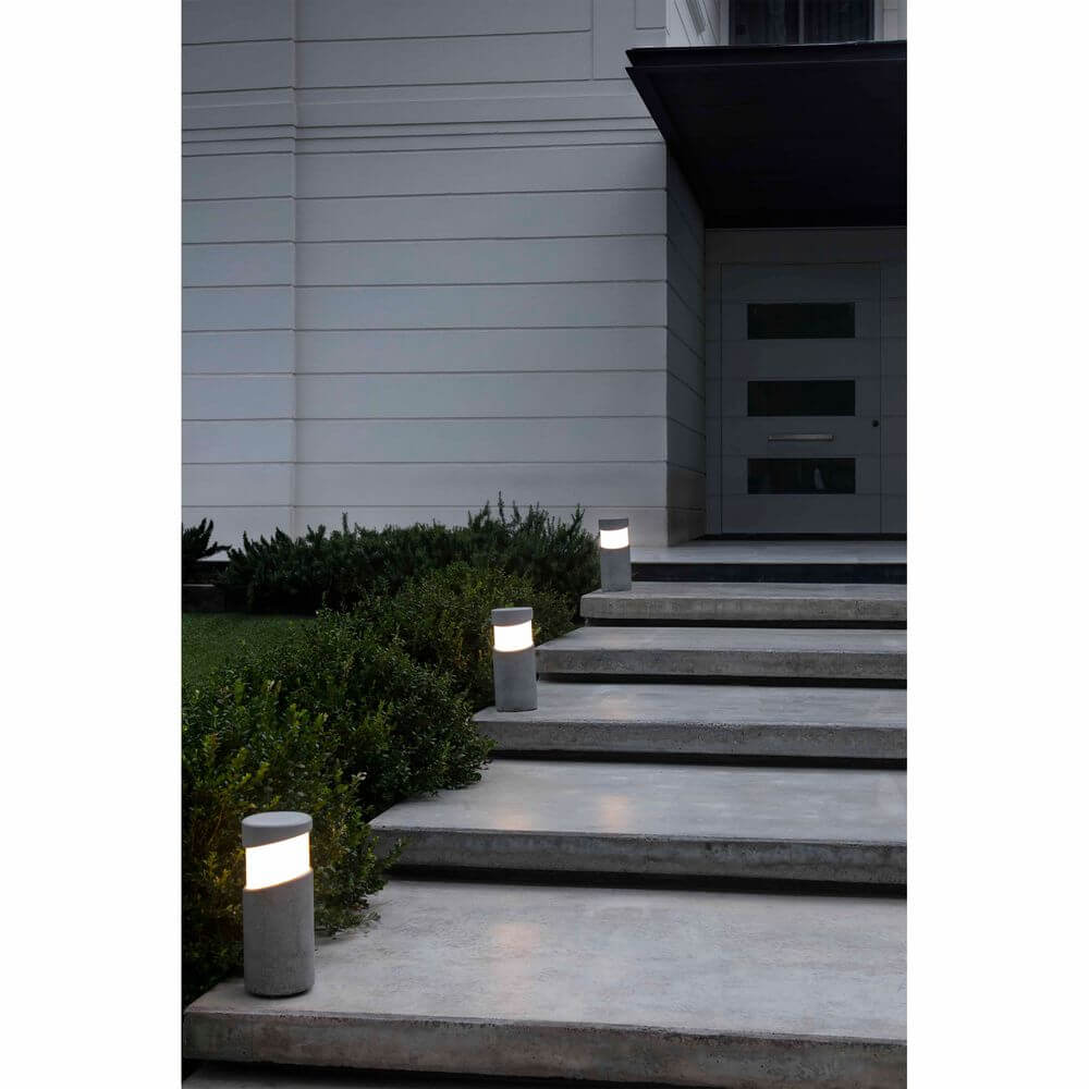 Sockelleuchte BLOCK IP65 Zementgrau beleuchtet Eingangstreppe und Gartenlandschaft.