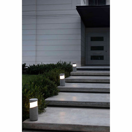Sockelleuchte BLOCK IP65 Zementgrau beleuchtet Eingangstreppe und Gartenlandschaft.